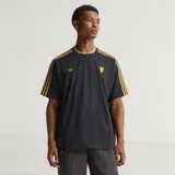 Camiseta de fútbol Adidas del Manchester United, modelo Terrace Icons. Diseño negro con sutiles rayas verticales moradas, franjas amarillas en los hombros y detalles bordados en dorado, incluyendo el trébol de Adidas y el escudo clásico del club.