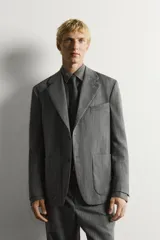 Blazer de corte relaxed fit de Zara, confeccionado en 100% lana color gris. Cuenta con cuello de solapas de muesca, manga larga, bolsillos de parche en la cadera, bolsillo de vivo en el pecho y cierre frontal con un botón.