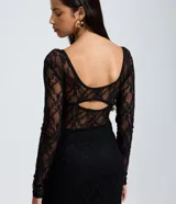Vestido midi de encaje negro con mangas largas, escote en V estructurado y detalle de recorte tipo corset en el torso. La falda presenta un diseño con transparencia y caída fluida.