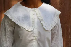 Camisa blanca de algodón con cuello bebé grande, detalle de volados en los bordes y mangas largas con bordado inglés.