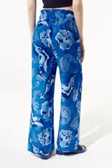 Pantalón fluido de corte flare con pretina elástica, estampado con flores, estrellas y otros motivos en tonos azules.