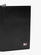 Billetera plegable Tommy Hilfiger confeccionada en piel negra con textura acanalada. Presenta un logo esmaltado distintivo de la marca en la parte frontal.