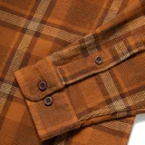 Camisa de franela marrón a cuadros con dos bolsillos frontales con solapa abotonada, de manga larga y corte clásico.