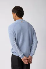 Sweater de punto grueso con textura waffle, de calce relajado y cuello redondo. Presenta puños y ruedo acanalados, con un pequeño parche con logo en el puño izquierdo.