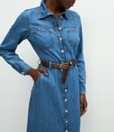 Vestido midi de denim con cuello camisero, mangas largas con puños abotonados y cierre frontal completo con botones metálicos. Presenta bolsillos aplicados en el pecho y un corte recto estructurado.