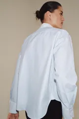Camisa de algodón con cuello solapa y puños en color blanco a contraste. Presenta cierre frontal con alamares negros y bajo asimétrico redondeado.