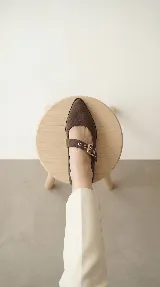 Zapato tipo Mary Jane de gamuza color marrón, con taco cuadrado medio y tira ajustable con hebilla metálica y ojalillos decorativos.