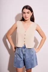 Chaleco color crema de tejido de punto, con escote en V y cierre frontal con botones.