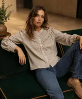 Camisa de manga larga color beige con diseño en relieve, detalles de volados y frunces en el frente y hombros, cierre frontal con botones y cuello mao.