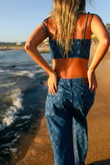 Top corto de denim azul con estampado de monogramas, escote recto, breteles finos y cierre en la espalda.