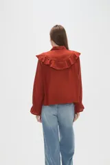Camisa de algodón blanca con cuello camisero, cierre frontal de botones y volados bordados en el frente y hombros. Presenta mangas largas con puños acampanados y detalles bordados en el ruedo.