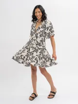 Vestido corto de viscosa en color beige con estampado floral en negro, escote en V con botones frontales, mangas cortas y falda amplia con volados en capas.