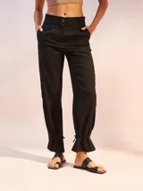 Pantalón de tiro alto color negro, confeccionado en mezcla de lino. Presenta corte recto con pinzas en la cintura, bolsillos laterales y un detalle de ajuste con lazo en los tobillos que crea un efecto acampanado.
