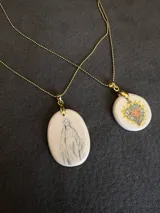 Collar de cadena fina dorada con dije ovalado de cerámica en tono crema, ilustrado con la figura de la Virgen.