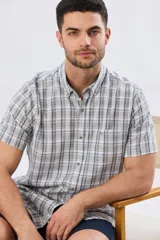 Camisa de manga corta confeccionada en mezcla de lino y algodón, con diseño a cuadros en tonos gris, blanco y azul. Presenta cuello camisero con botones y bolsillo ojal en el pecho con detalle bordado.
