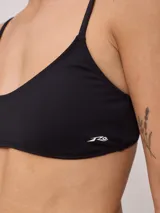 Top de bikini deportivo color negro, con escote redondo y breteles finos ajustables. Presenta el logo de la marca estampado en blanco en la parte inferior izquierda.