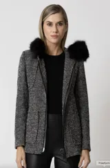 Abrigo de lana bouclé en blanco y negro, con corte recto, bolsillos amplios y cierre metálico frontal. Detalle de piel sintética negra en los hombros.