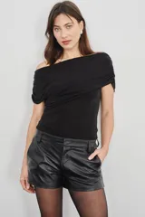 Blusa asimétrica negra con diseño drapeado envolvente de hombros descubiertos y manga corta.