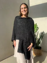 Ruana tejida en punto jersey, color negro con destellos brillantes de lurex. Presenta una etiqueta de cuero sintético con logo en la parte posterior.