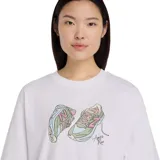 Remera blanca de manga corta con cuello redondo y estampado de zapatillas New Balance en tonos pastel.
