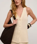 Chaleco de punto color beige claro, con cuello en V y cierre frontal de botones. El tejido presenta un patrón texturizado de pequeños puntos.