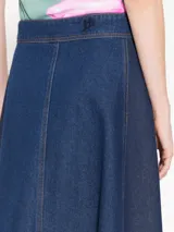 Pollera midi de denim azul con recortes laterales en denim más oscuro, acceso frontal con broches metálicos y bordado JCH en la cintura trasera.