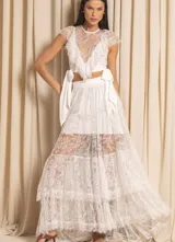 Falda larga de encaje blanco off-white, con capas superpuestas y forro que deja ver parcialmente la pierna. La cintura es ancha y lisa, con lazos laterales anchos.