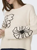 Sweater tejido de color beige con cuello redondo, mangas largas y detalles de bordado floral en negro.