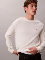 Remera de manga larga Calvin Klein de color blanco off-white, confeccionada en tejido de punto térmico con textura de nido de abeja. Presenta cuello redondo, puños acanalados y un pequeño logo bordado en el pecho.