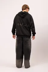 Campera oversize con capucha y cierre frontal metálico. Presenta bolsillos frontales con remaches metálicos y un diseño exclusivo en la espalda con la palabra "TACHA" formada por alfileres de gancho plateados. Confeccionada en tejido de jersey con interior suave.