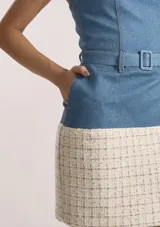 Vestido corto entallado con diseño bicolor, cuerpo superior de denim azul con escote strapless y cinturón integrado, y falda de tweed en tonos claros con textura. Cierre trasero con cremallera.