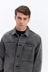Campera de jean de corte recto y lavado desgastado, con cuello clásico, cierre frontal con botones metálicos y un bolsillo grande aplicado en el pecho.