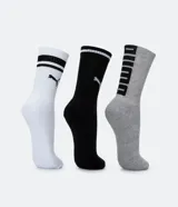 Kit de tres pares de medias deportivas Puma de caña larga. Un par es beige con dos rayas marrones y logo de Puma. Otro par es blanco liso. El tercer par es marrón oscuro con dos rayas blancas y logo de Puma. Todas están confeccionadas en algodón.