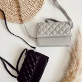 Cartera bandolera negra de ecocuero con diseño acolchado en rombos. Tiene asa corta superior y correa larga desmontable y regulable.