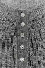 Jersey de punto color gris, con cuello redondo y abertura frontal con botones. Presenta mangas largas raglán y puños y bajo acanalados.