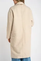 Tapado largo de corte oversize en color beige, con solapas clásicas y cierre frontal con botones. Presenta un diseño minimalista y elegante, ideal para un look sofisticado.