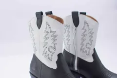 Botas de estilo western (texanas) de caña media, color blanco, confeccionadas en cuero. Presentan bordados decorativos en la caña y puntera cuadrada. Cuentan con cierre lateral y taco de altura media.