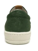 Zapato slip-on verde oscuro de gamuza con perforaciones, suela blanca y elástico lateral.