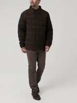Chaqueta de lana Harris Tweed con patrón de tartán en tonos verdes, marrones y detalles en burdeos. Presenta cuello camisero, cierre frontal con botones, bolsillos de parche y acolchado interior térmico.