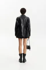 Chaqueta semi-larga negra con acabado brillante o efecto charol, cuello camisero y frunce ajustable en la cintura. Presenta cierre frontal y bolsillos prácticos.