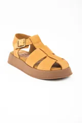Sandalia tipo guillermina de cuero color camel, con diseño de tiras anchas entrelazadas, cierre con hebilla metálica lateral y suela de plataforma plana en tono marrón.