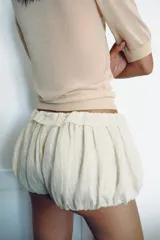 Top de punto fino semitransparente, color beige, con escote redondo y mangas cortas con puños ajustados.