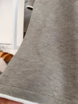 Remera tejida de manga corta con cuello redondo, confeccionada en una mezcla de poliéster, acrílico, poliamida y lana. Presenta un diseño de calce recto en color marrón con detalles de terminaciones en contraste de color blanco en el cuello, las mangas y el ruedo.