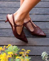 Zapato slingback tipo Oxford color marrón con textura efecto croco, punta fina, taco aguja bajo y tira ajustable al talón con hebilla metálica.
