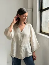 Camisa de lino color beige, de corte holgado, con escote en V y cierre frontal de botones.