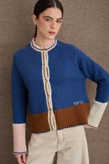 Cardigan de punto con diseño color block en tonos azul, marrón y crema. Presenta cuello redondo, cierre frontal con botones, mangas largas con puños en contraste y detalle bordado en el frente.
