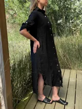 Vestido camisero largo de lino blanco, con cuello camisero, manga corta enrollada y cierre frontal de botones de nácar. Presenta aberturas laterales en el bajo.