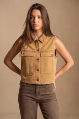 Chaleco de denim color camel con efecto lavado, cuello camisero, cierre frontal con botones metálicos y dos bolsillos frontales con solapa.