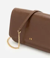 Cartera bandolera Satinato pequeña de color marrón oscuro, confeccionada en poliuretano con detalles de herrajes dorados y correa larga de cadena. Cuenta con solapa frontal y múltiples compartimentos internos.