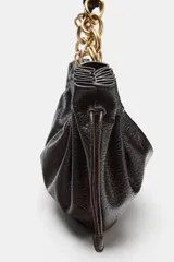 Bolso de hombro en color marrón oscuro con efecto craquelado. Presenta detalles fruncidos en los laterales con tiradores ajustables y un asa corta que combina una parte de material sintético con eslabones de cadena metálica dorada. Cuenta con un bolsillo interior y cierre mediante cremallera.